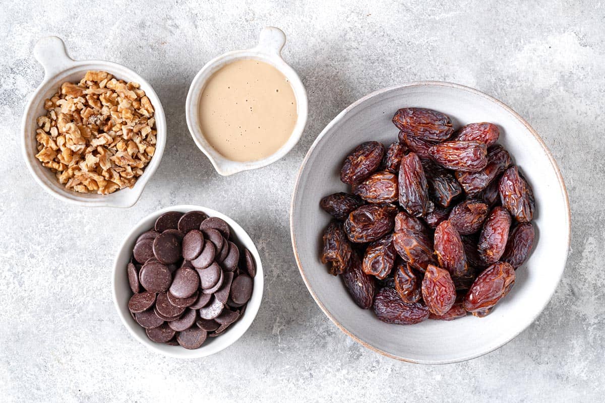 ingredients for chocolate covered date bars including chopped walnuts, large Medjool dates, tahini, and dark chocolate chips.